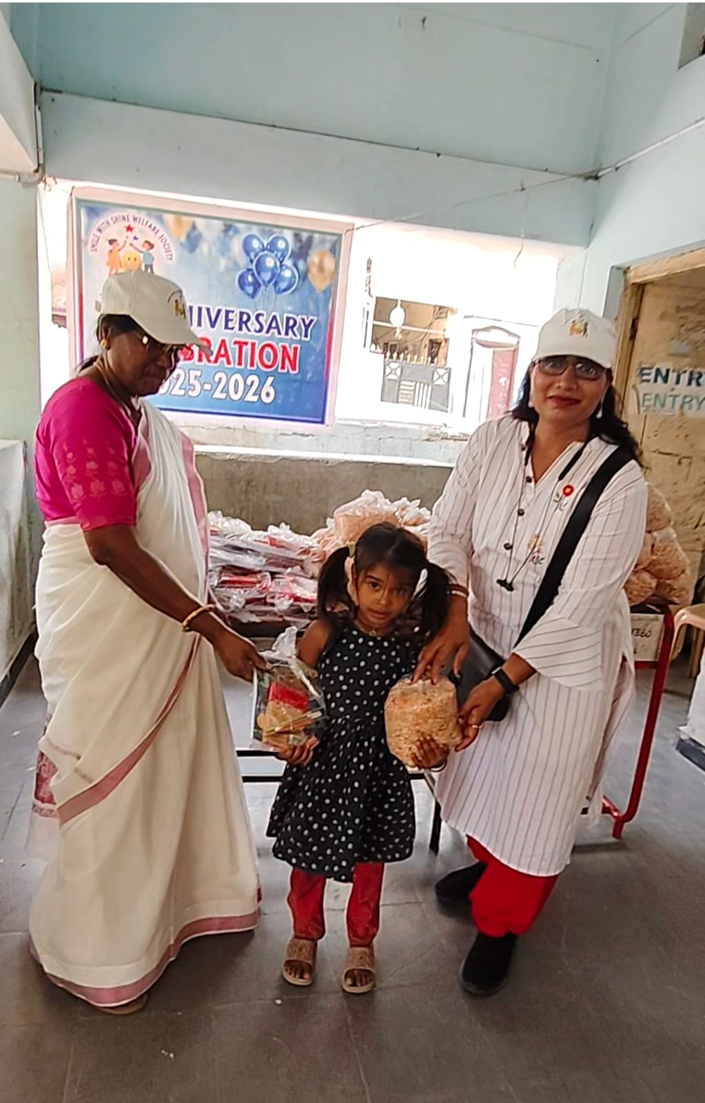 Founder Smt. Grace Mani and a team member handing over a kit to a young girl at the Smile With Shine 1st Anniversary stationery drive